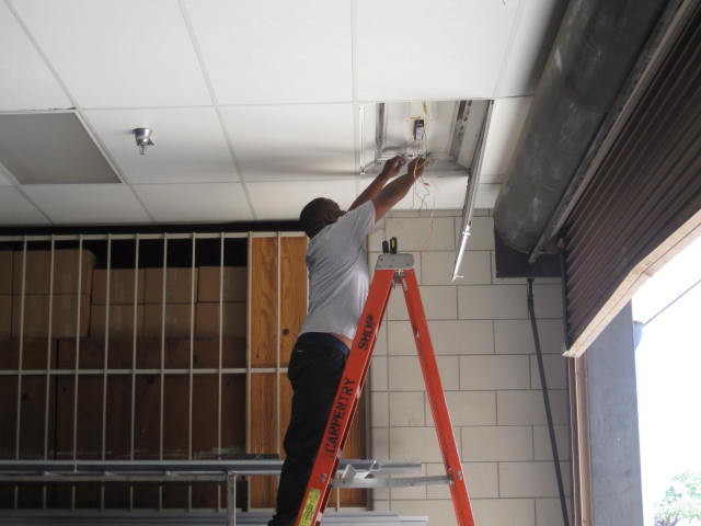 A Person fixing the wires on sealing using a lader